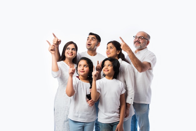 Indn famille multigénérationnelle pointant ou présentant un espace vide, debout isolé contre un mur blanc