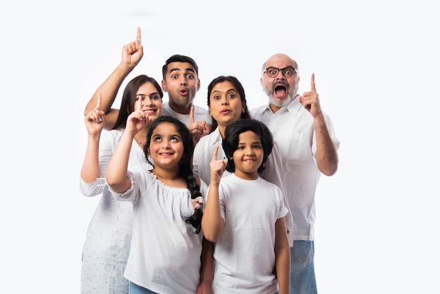 Indn famille multigénérationnelle pointant ou présentant un espace vide, debout isolé contre un mur blanc