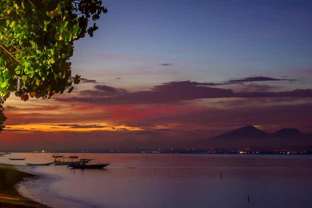 Indonésie. Baie tropicale avec bateaux sur eau calme. Ciel coloré après le coucher du soleil