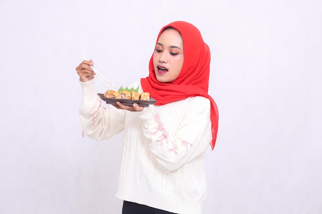 indonésie femme portant un hijab regarde le bas avec des baguettes et porte une assiette contenant