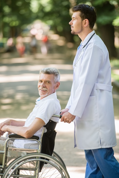 Infirmier marchant avec patient senior en fauteuil roulant.