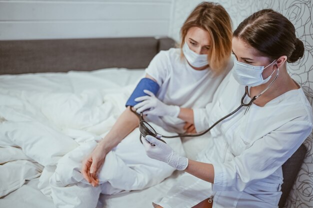 Un infirmier en masque protecteur mesure la pression artérielle avec un sphygmomanomètre. Concept de coronavirus (COVID-19). Premiers symptômes. Femme malade d'une infection virale grippale en quarantaine d'isolement à domicile