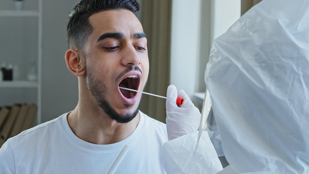 Photo un infirmier méconnaissable, un travailleur médical effectuant un test pcr avec un équipement pour le coronavirus covid-19 à un homme ethnique. un homme espagnol, un homme arabe, un patient ouvre la bouche et donne un échantillon de salive pour le virus de l'infection.