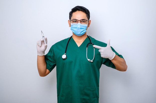 Infirmier ou médecin sérieux en gommage vert masque médical pointant vers la seringue avec le vaccin contre le coronavirus