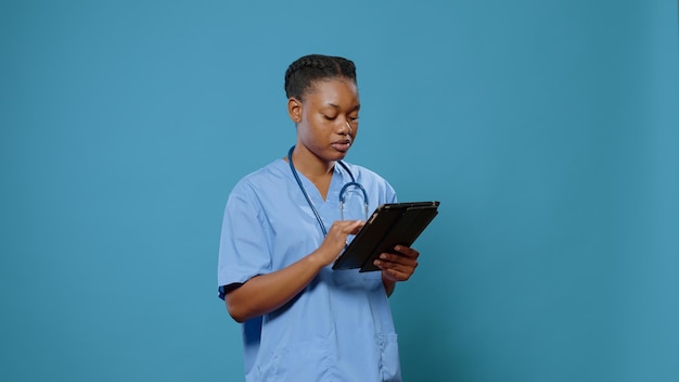 Infirmière afro-américaine en uniforme utilisant une tablette numérique pour pratiquer la médecine et les soins de santé. Assistant médical travaillant avec des gadgets et de la technologie, ayant un stéthoscope et une expertise.