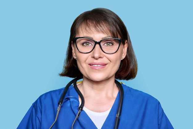 Infirmière d'âge moyen en uniforme bleu avec stéthoscope souriant regardant la caméra