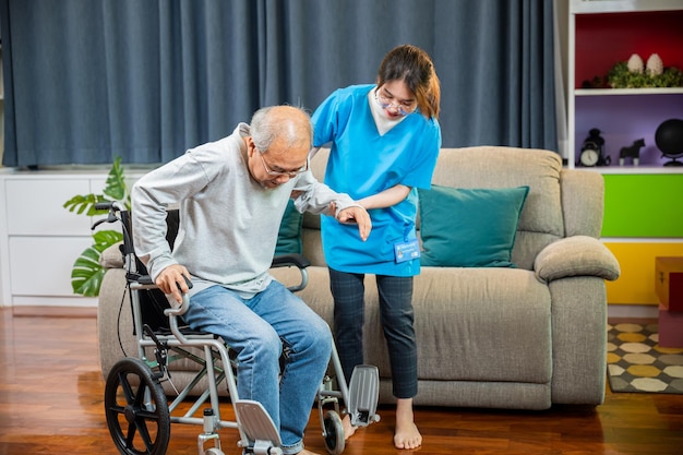 Une infirmière asiatique aide un homme âgé à se lever du fauteuil roulant pour s'entraîner à marcher.