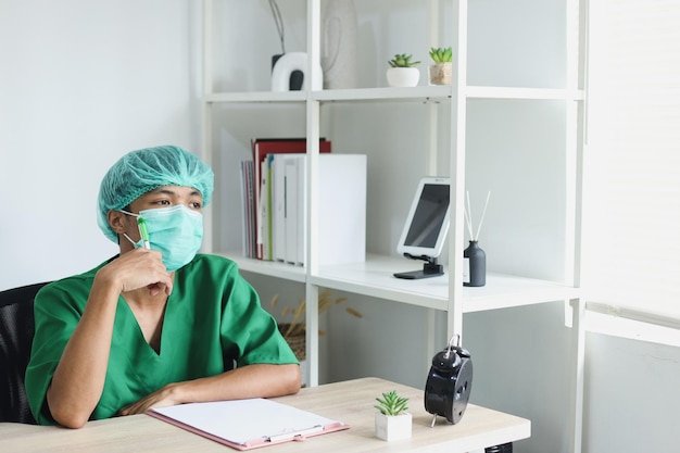 Infirmière asiatique réfléchie portant un masque facial et regardant la fenêtre avec une expression de visage pensif