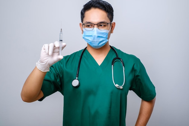 Infirmière asiatique sérieuse portant un masque médical, des gants en caoutchouc et des gommages à la recherche d'une seringue avec vaccin