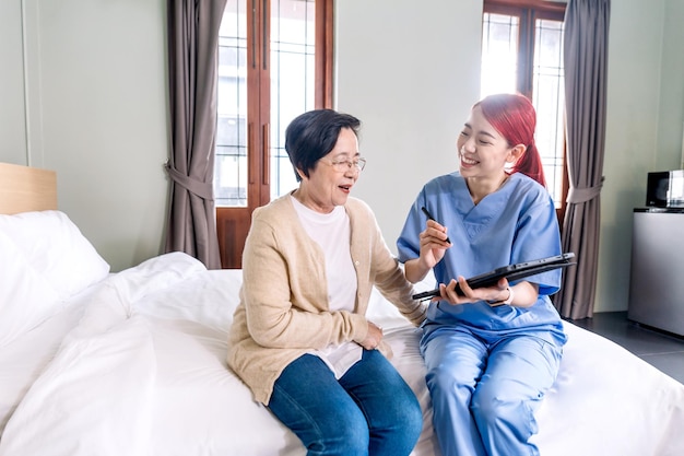 Une infirmière asiatique en thérapie portant des gommages signale l'état de santé d'une femme asiatique âgée avec une tablette numérique dans la chambre Visite d'un soignant à domicile Concept de soins de santé à domicile et de maison de retraite