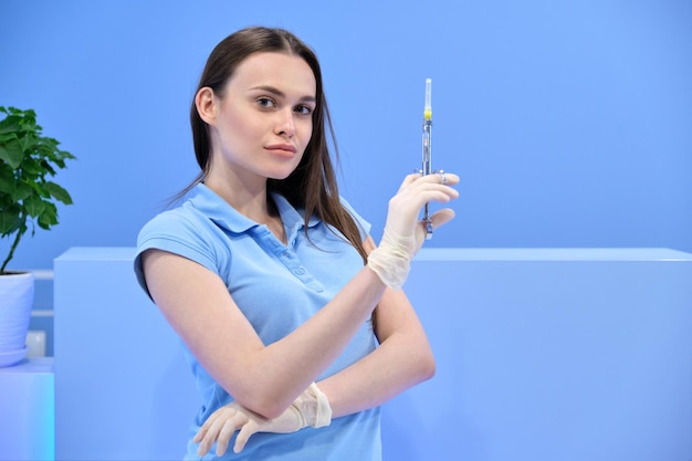 Infirmière de la belle jeune femme avec seringue, femme médecin en uniforme regardant la caméra, clinique de fond bleu