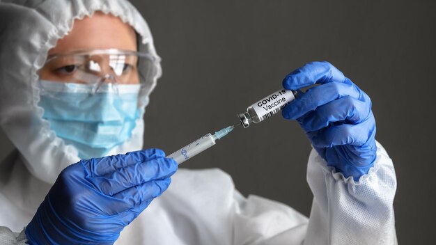 Une infirmière en costume médical EPI tient une seringue et une bouteille avec un vaccin pour la guérison du COVID19