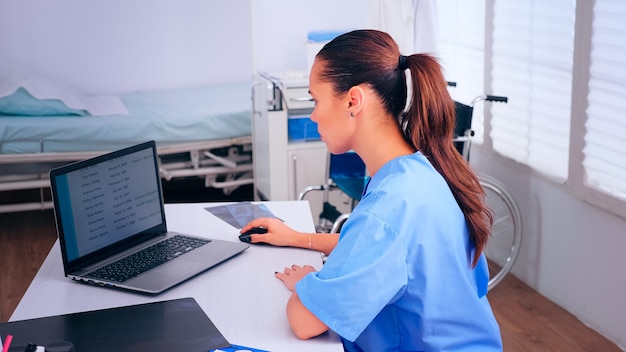 Infirmière du médecin tapant sur un ordinateur portable assis au bureau dans le cabinet, analysant les rendez-vous des patients. Médecin en médecine rédige une liste uniforme de patients consultés et diagnostiqués, faisant des recherches.