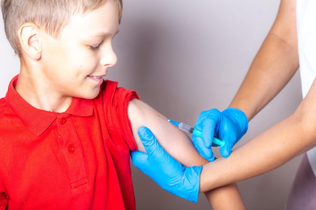 Une infirmière en gants bleus injecte un vaccin à l'aide d'une seringue dans l'épaule de l'enfant