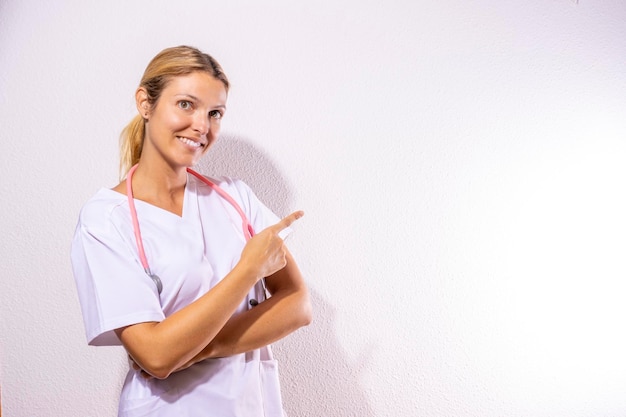 Infirmière habillée en chemise d'hôpital et stéthoscope pointant Concept sanitaire Fond blanc et espace de copie