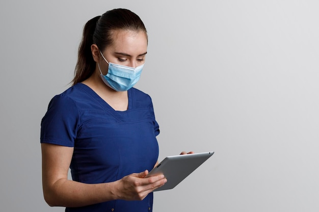 Infirmière latina avec masque assis travaillant avec tablette numérique