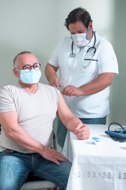Une infirmière latino-américaine injecte un vaccin à un homme hispanique âgé dans le bras à l'aide d'une seringue et d'une solution médicale
