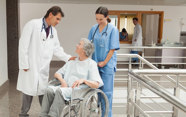 Infirmière et médecin parlant avec une vieille femme en fauteuil roulant