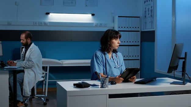 Infirmière médicale analysant l'expertise des soins de santé des patients sur ordinateur en comparant avec le rapport de données sur tablette, travaillant tard dans la nuit au bureau de l'hôpital. Service et concept de médecine