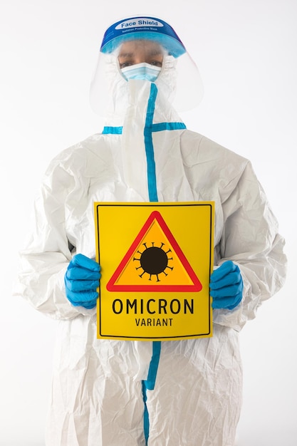 Infirmière médicale en équipement de protection individuelle et gants en latex, tenant une pancarte jaune avec un symbole de danger qui se lit comme suit : 'VARIANT OMICRON'. Concept de coronavirus, de pandémie et de santé.