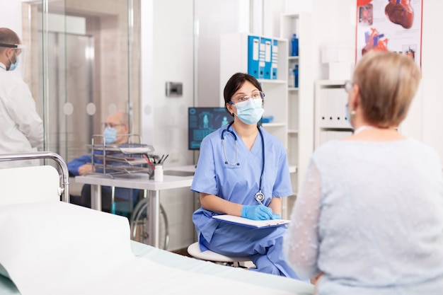 Infirmière médicale parlant avec une femme âgée infectée par covid19 au cours d'un examen