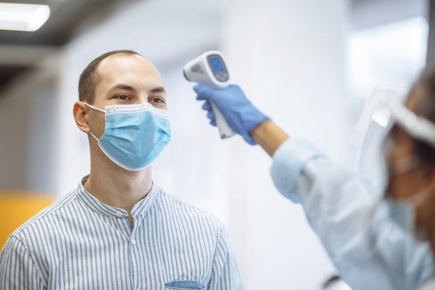 L'infirmière mesure la température d'un patient à l'hôpital avec un thermomètre sans contact. Les personnes portant des masques médicaux de protection. Concept de prévention et de soins de santé de coronavirus.