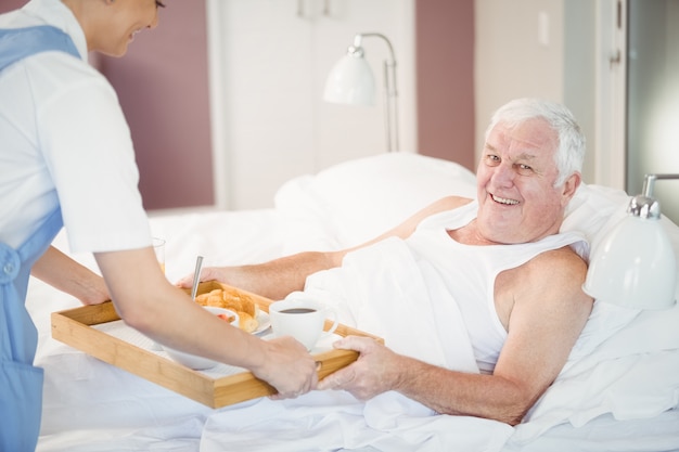 Infirmière offrant le petit déjeuner à un homme âgé allongé sur un lit