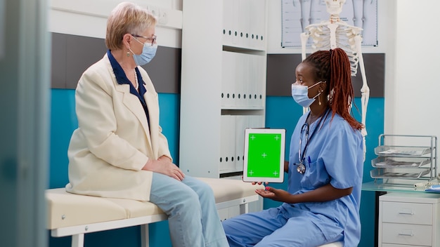 Infirmière et patient avec masque facial regardant un écran vert sur une tablette numérique, faisant des consultations au bureau. Assistant tenant l'écran avec modèle chromakey isolé et espace de copie vierge.