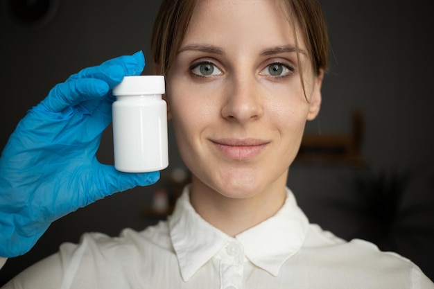 Une infirmière portant des gants médicaux bleus tient une bouteille de pilules