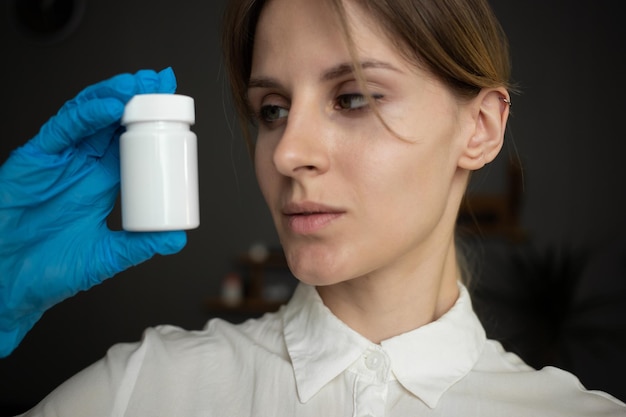 Une infirmière portant des gants médicaux bleus tient une bouteille de pilules