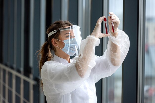 Infirmière portant des gommages tenant et regardant le tube à essai de sang en laboratoire