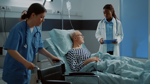 Infirmière préparant le fauteuil roulant pour le patient malade dans la salle d'hôpital