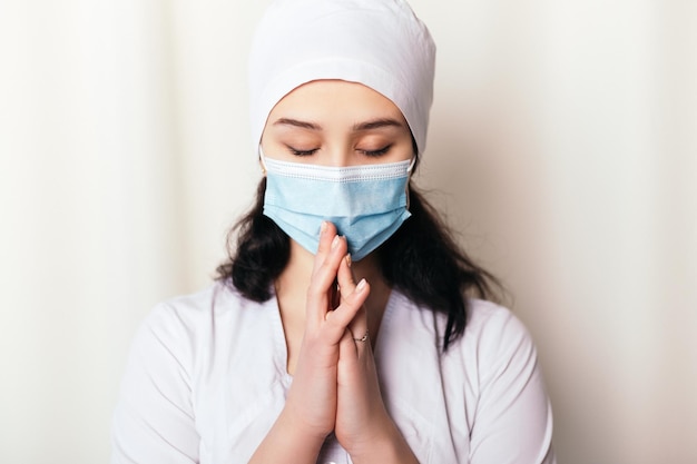 Infirmière en prière vêtue d'une blouse médicale et portant un masque facial