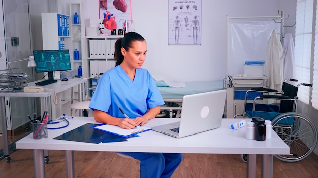 Photo infirmière recevant les résultats de santé des patients, prenant des notes sur le presse-papiers, lisant sur un ordinateur portable à l'hôpital. médecin en médecine rédigeant une liste uniforme de patients consultés et diagnostiqués, faisant des recherches