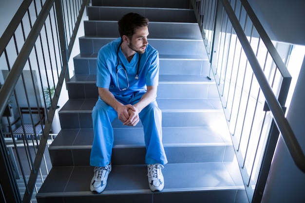 Infirmière réfléchie assis sur un escalier