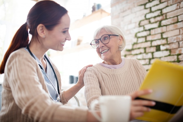 Infirmière rousse souriant tout en parlant à la gentille femme âgée lisant le livre