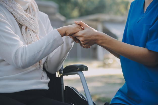 Une infirmière s'occupe d'un homme âgé en fauteuil roulant dans son jardin à la maison