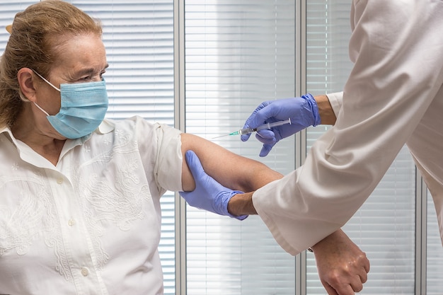 Infirmière avec une seringue tenant le bras d'une femme âgée avec un masque à vacciner