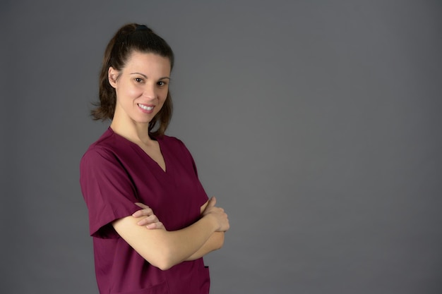Infirmière souriante avec les bras croisés posant sur le côté dans des gommages violets sur fond gris avec espace copie