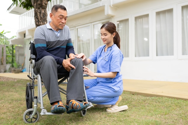 Une infirmière souriante et un homme âgé assis dans un fauteuil roulant dans le jardin