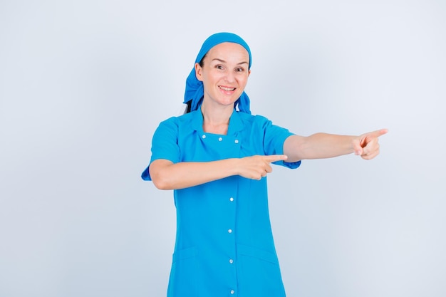 Infirmière souriante pointe vers la droite avec les index sur fond blanc