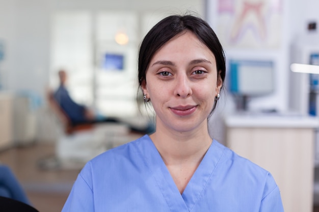 Infirmière souriante en stomatologie regardant à l'avant dans la zone d'attente du bureau du dentiste, homme âgé en attente d'un examen de santé des dents