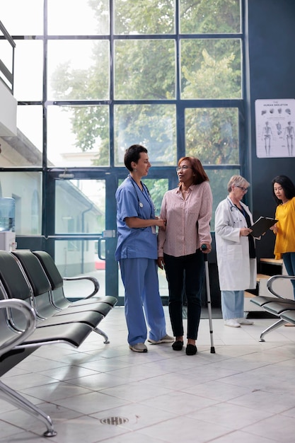 Photo infirmière soutenant une femme blessée essayant de marcher avec une canne, utilisant une aide à la marche pour récupérer après une fracture de la jambe. assistant aidant un patient âgé à guérir sa condition physique, physiothérapie.