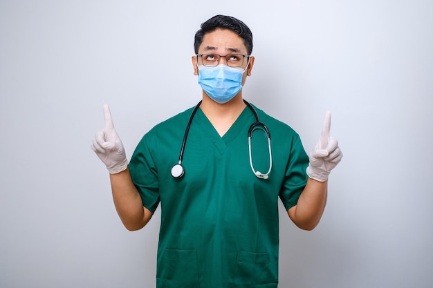 Infirmière surprise ou curieuse portant un masque médical gommage vert pointant les doigts vers le haut pour informer les patients sur la façon de prévenir l'infection corona