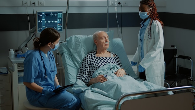 Infirmière avec tablette conseillant un patient malade dans un lit d'hôpital