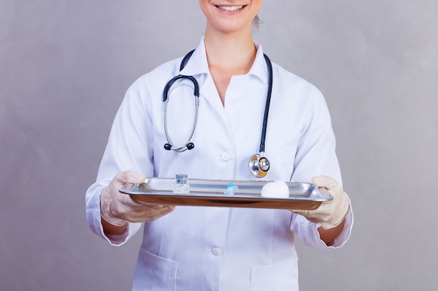 Infirmière tenant un plateau avec des médicaments sur fond gris. Médecins sur fond gris. Vaccin et médicament. Concept de santé et de soins