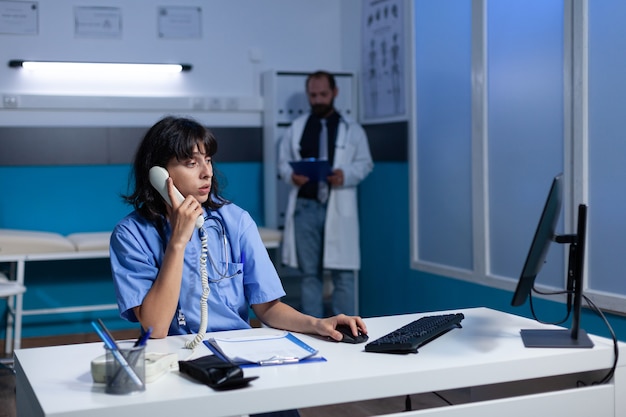 Infirmière en uniforme utilisant un téléphone fixe pour la conversation