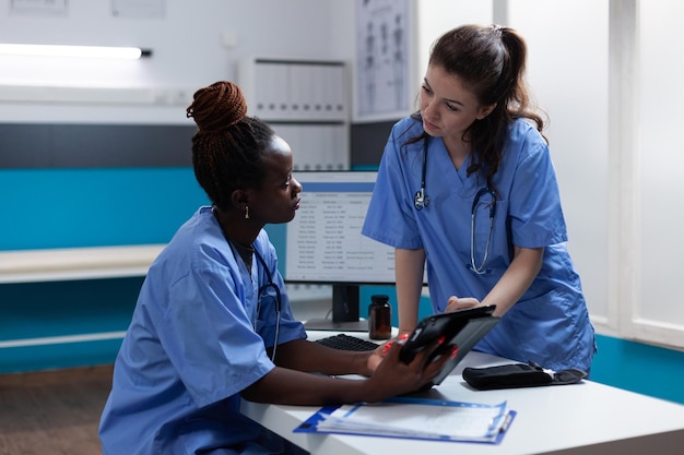 Photo infirmières médicales multiethniques analysant les symptômes de la maladie discutant des traitements de santé travaillant dans le bureau de l'hôpital. travail d'équipe vérifiant les médicaments pharmaceutiques sur l'ordinateur tablette assis au bureau