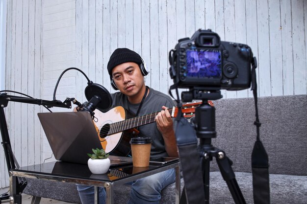 Influenceur asiatique jouant de la guitare lors d'un podcast ou d'une diffusion vidéo en direct pour le public, enregistré en fr