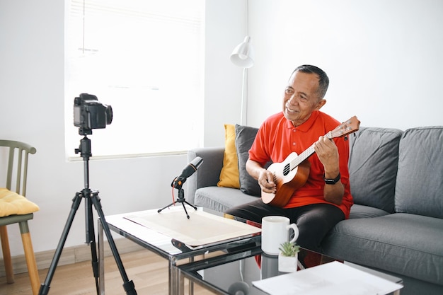 Influenceur asiatique senior homme jouant de la guitare pendant un podcast ou une diffusion vidéo en direct pour le public